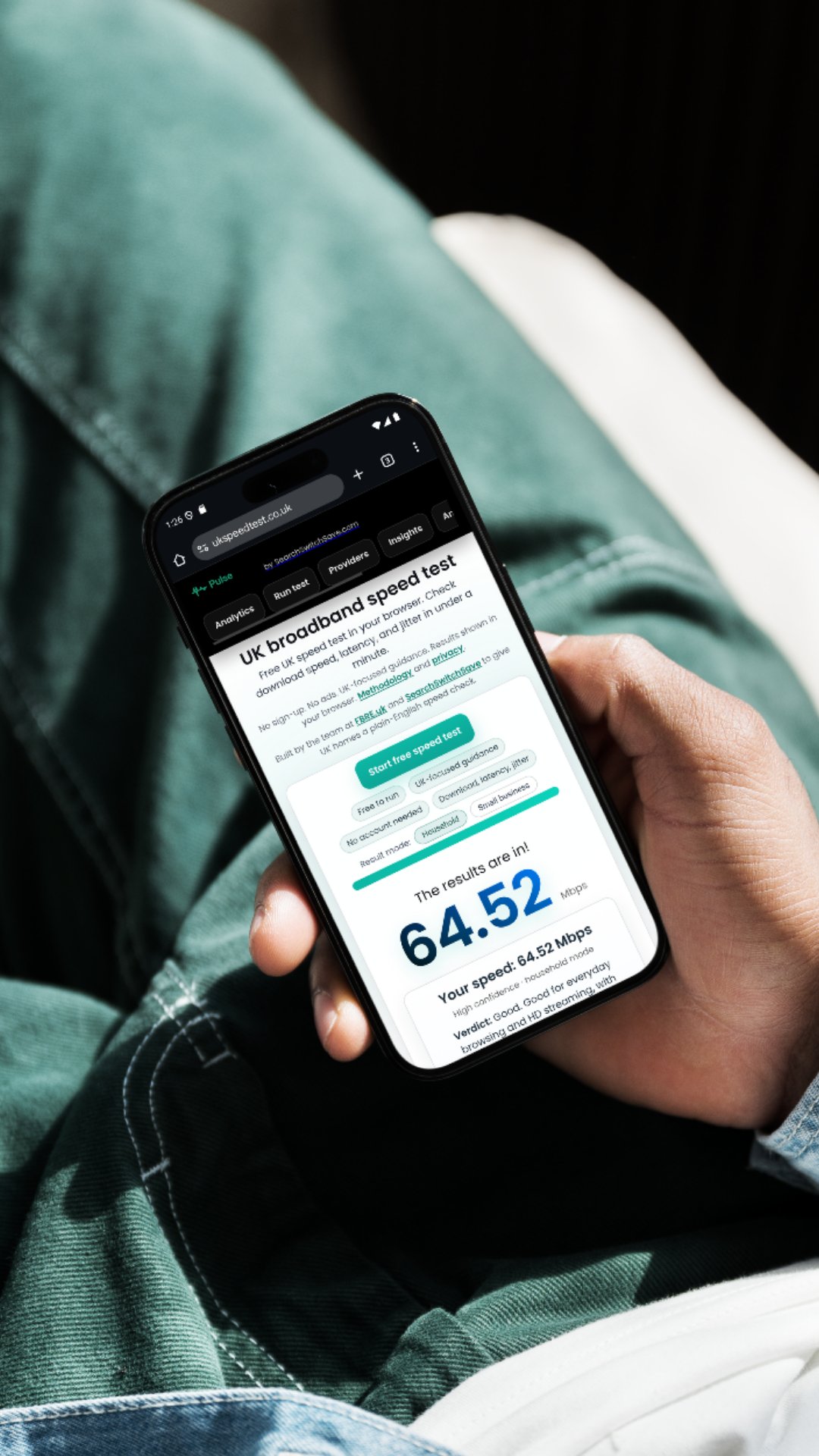 A person checking their UK broadband speed using UKSpeedTest.co.uk on a smartphone, showing a download speed of 64.52 Mbps