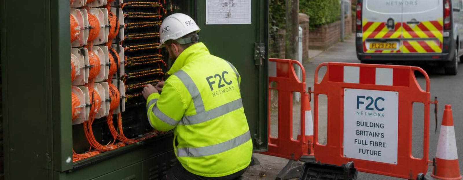 A fibre engineer working inside a street cabinet filled with spools of orange fibre cable on a residential road.