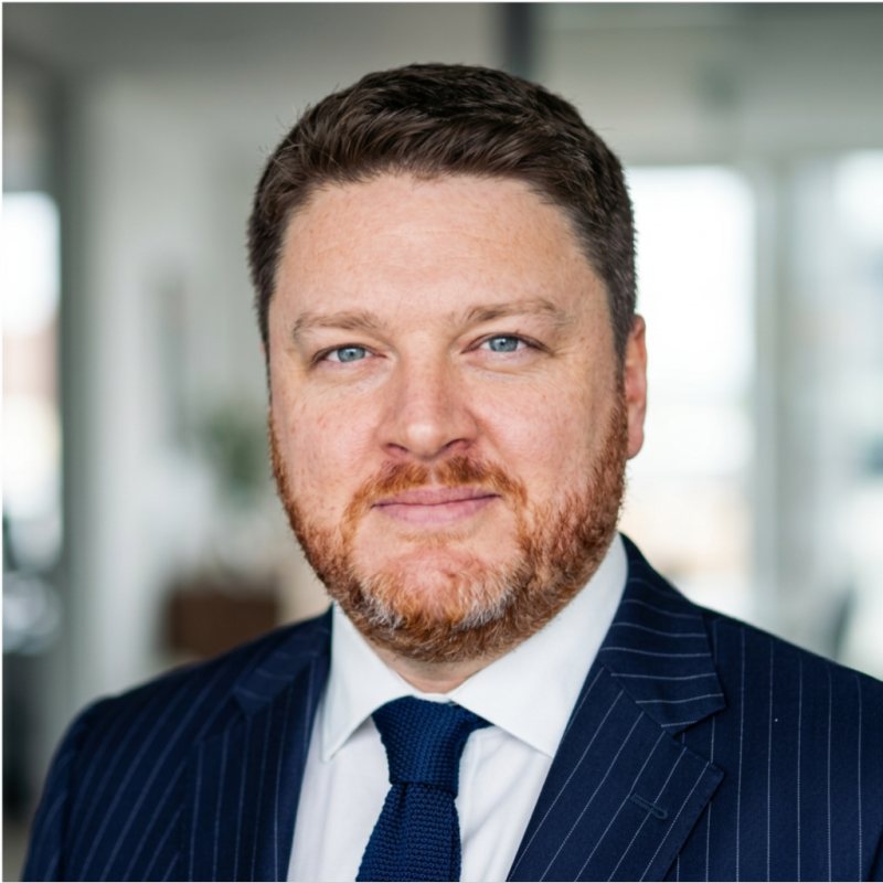 Professional headshot of Dr Alex J. Martin-Smith in a navy pinstripe suit