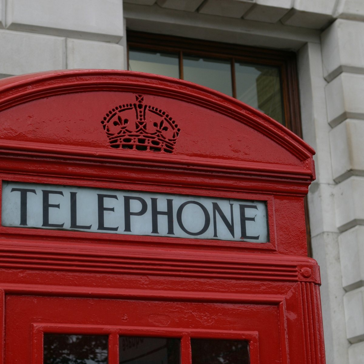 Close up of a red telephone box dome with pierced crown and TELEPHONE sign against a stone building
