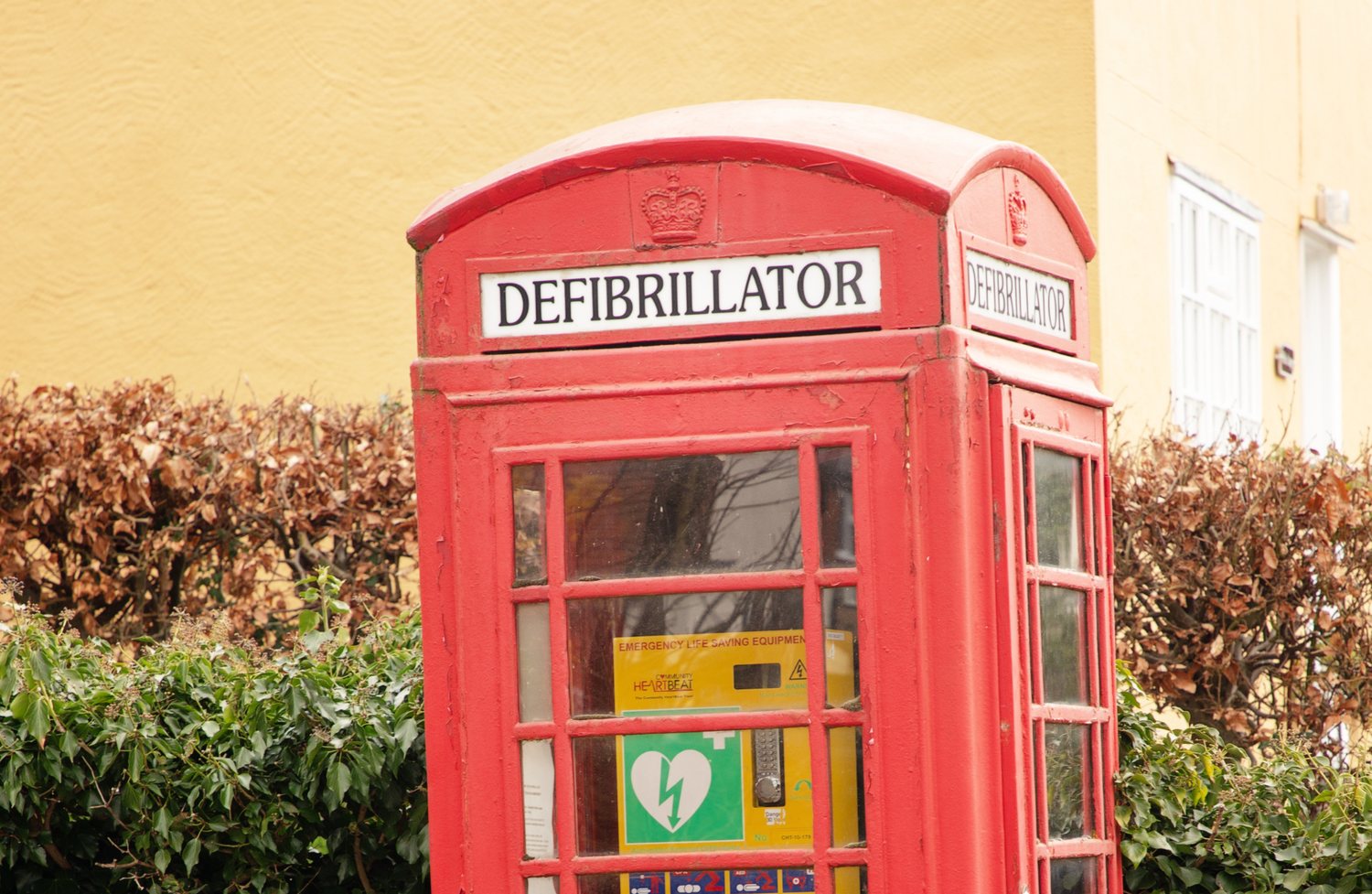 Red telephone box converted to a public defibrillator station, with DEFIBRILLATOR signage and emergency equipment visible