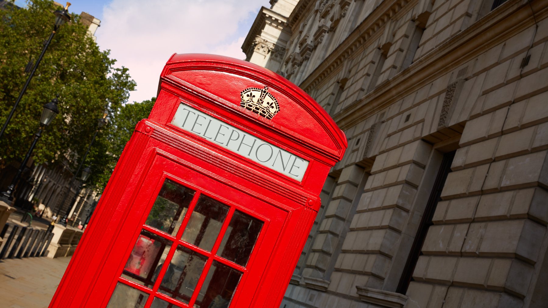 Tilted view of a glossy red telephone box against a grand stone facade