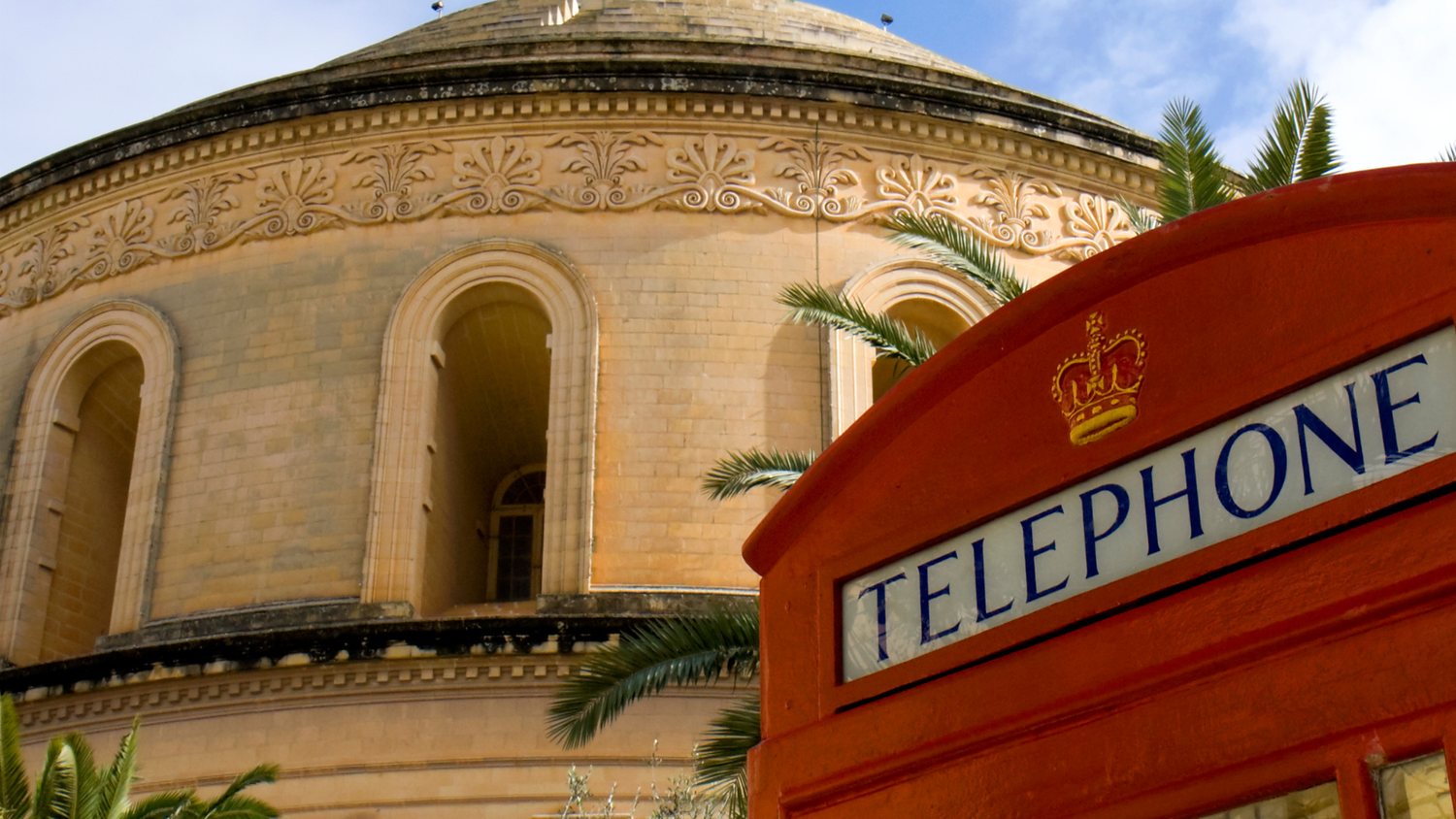 Red telephone box with a crown motif in front of the Mosta Rotunda dome in Malta