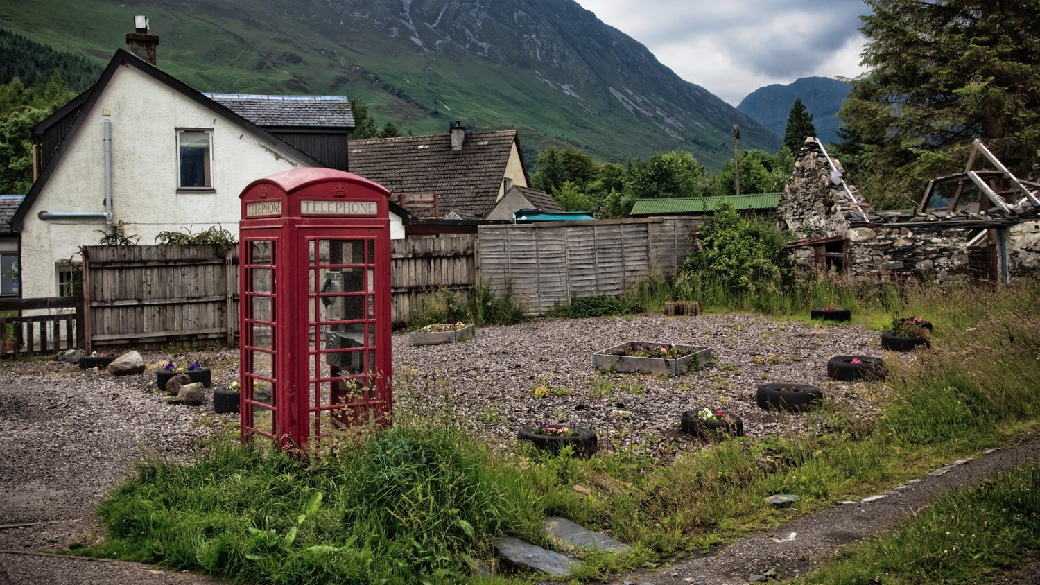 Weathered red K6 telephone box in a small mountain village with steep green slopes behind