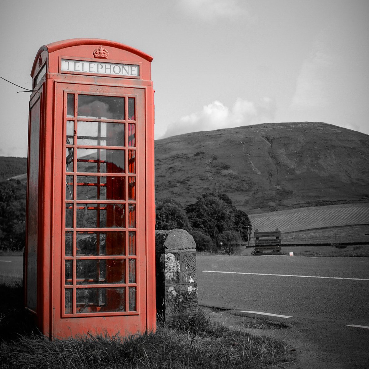 Selective colour image of a red telephone box against a monochrome hillside road