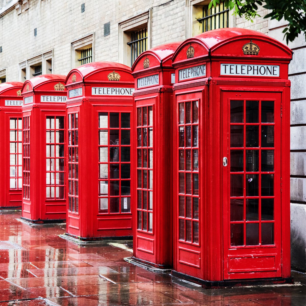 Five red telephone boxes standing in a line on a wet pavement